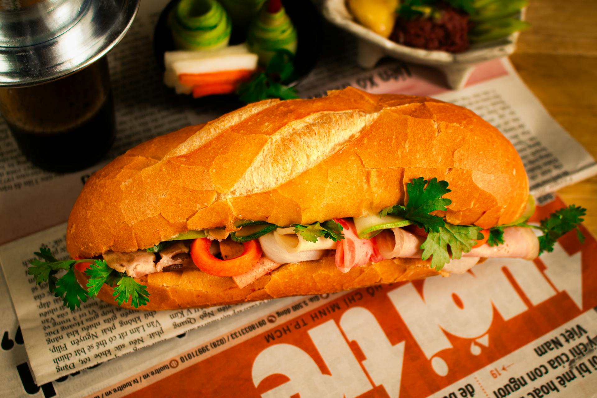 Crispy golden-brown Vietnamese bánh mì filled with meats and cilantro, resting on a traditional Tuổi Trẻ newspaper background.