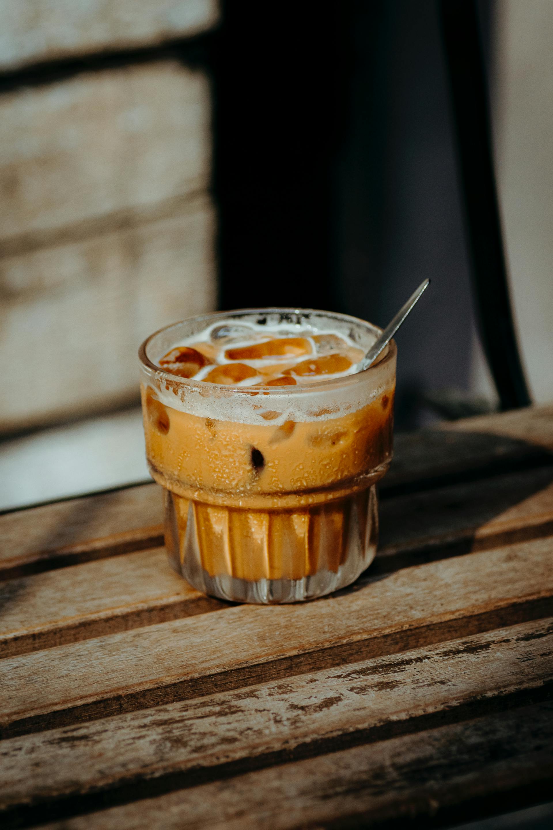 A glass of creamy Vietnamese iced milk coffee with condensation and ice cubes on a rustic wooden table.