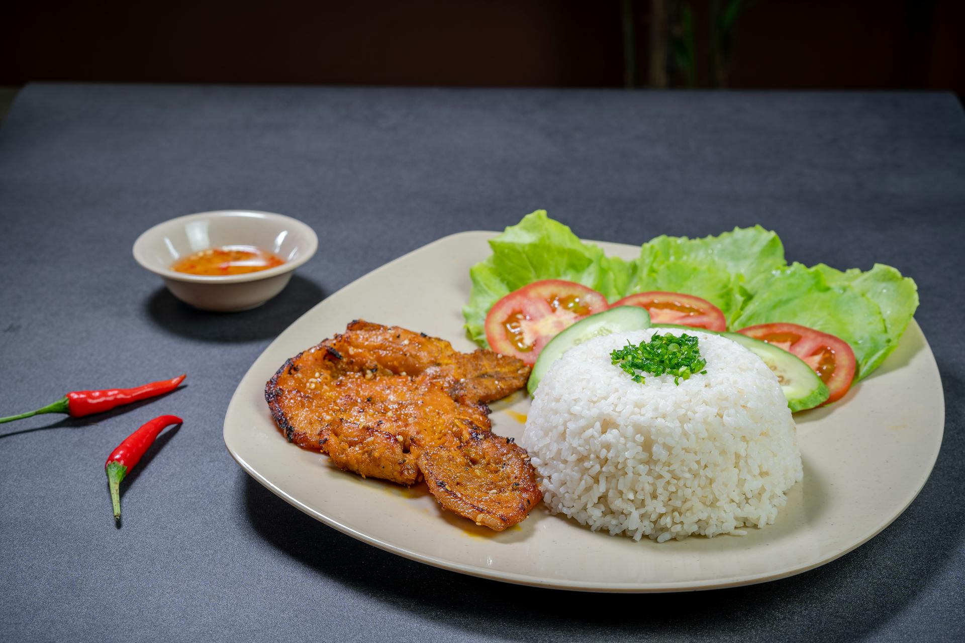 Vietnamese broken rice featuring a grilled pork chop, fresh vegetables, scallion oil, and a side of chili fish sauce.