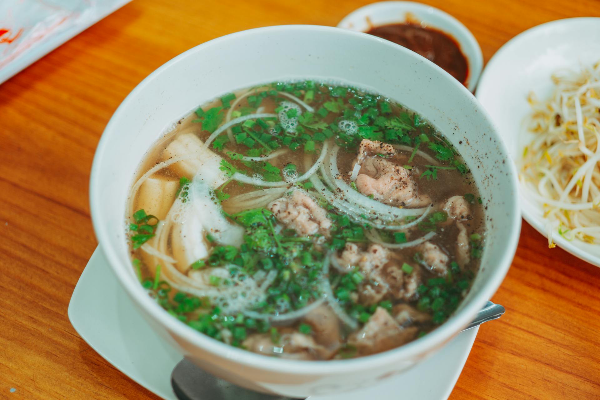 Traditional Vietnamese beef phở in a white bowl with aromatic broth, rice noodles, sliced meat, and fresh green scallions.