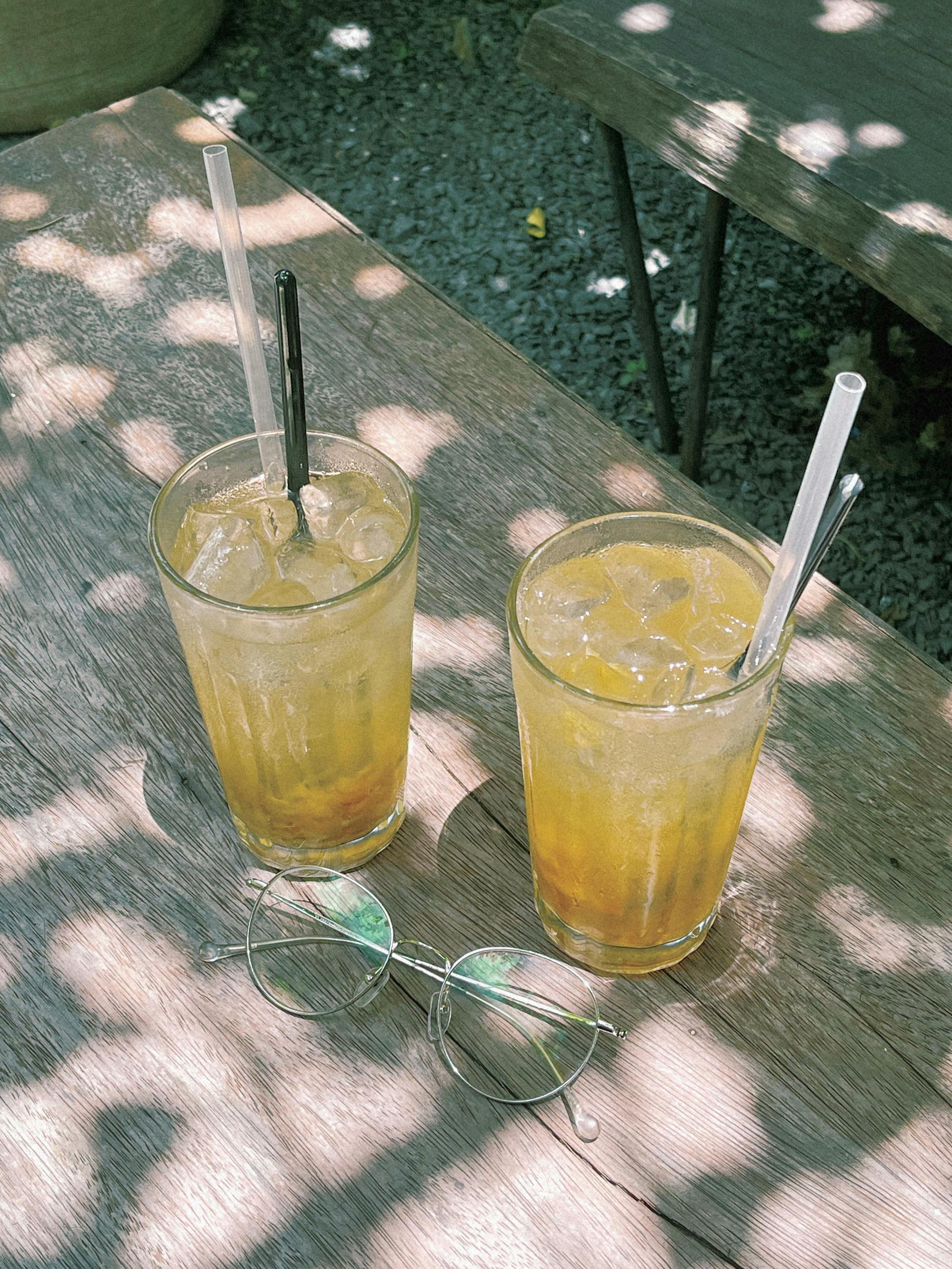 Two glasses of refreshing golden Vietnamese iced tea with ice on a rustic wooden table under dappled sunlight.