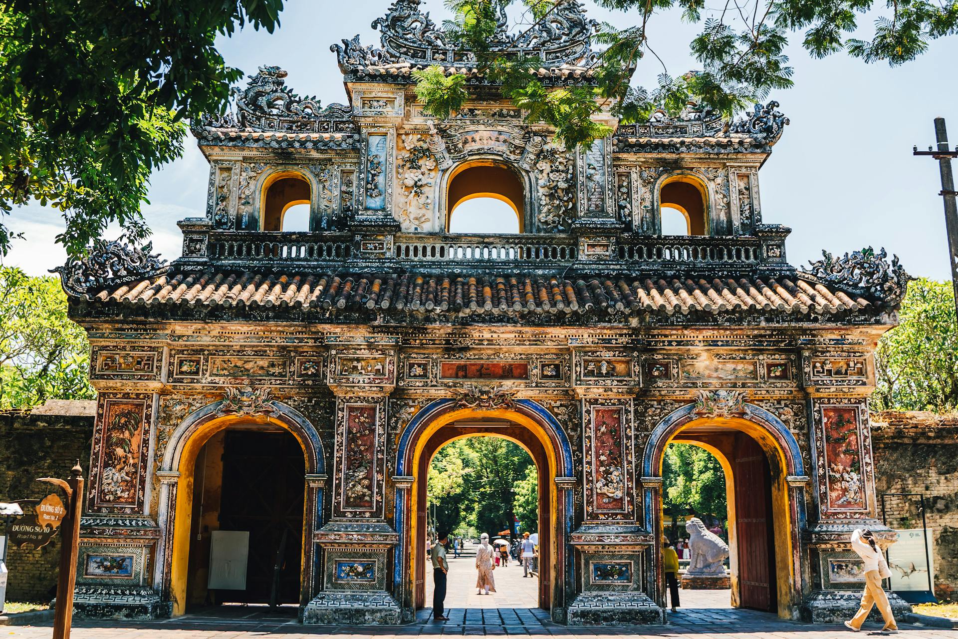 Intricately decorated imperial gate in Huế featuring vibrant ceramic mosaics, weathered yellow arches, and traditional tiered tile roofs.